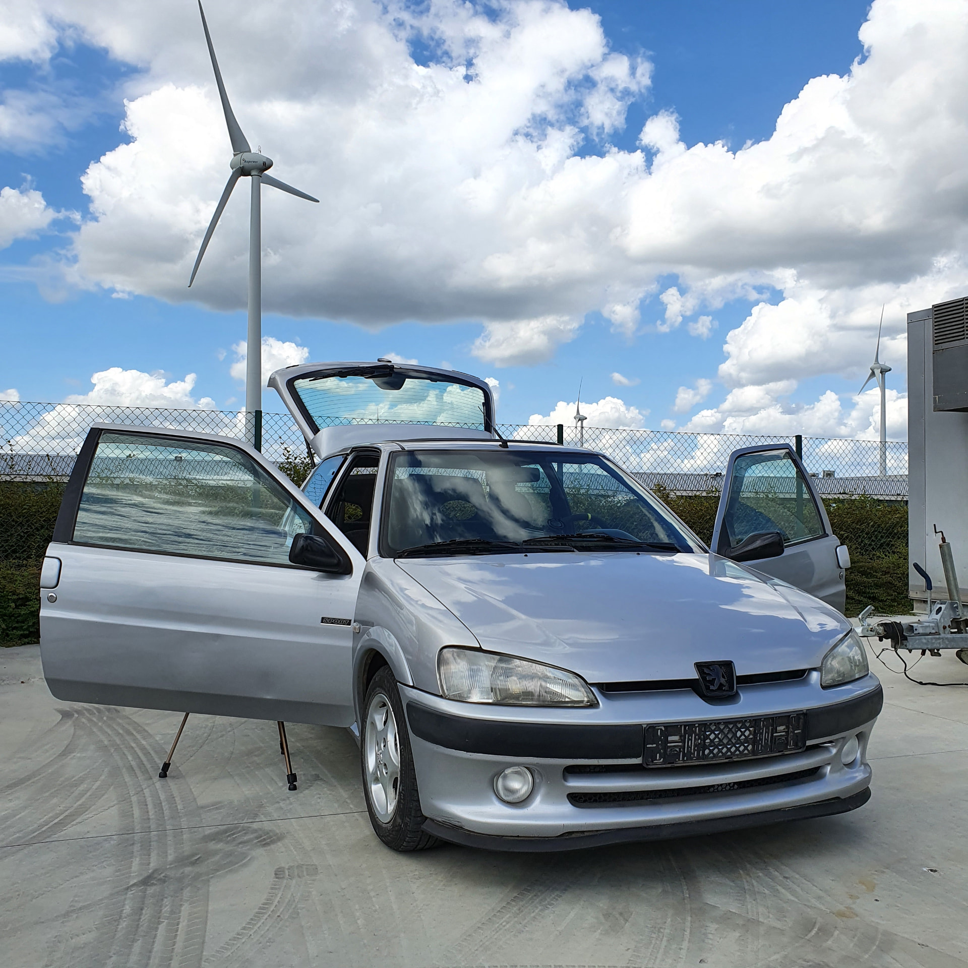 Peugeot 106 with its doors and hatch open, wind turbines in the background