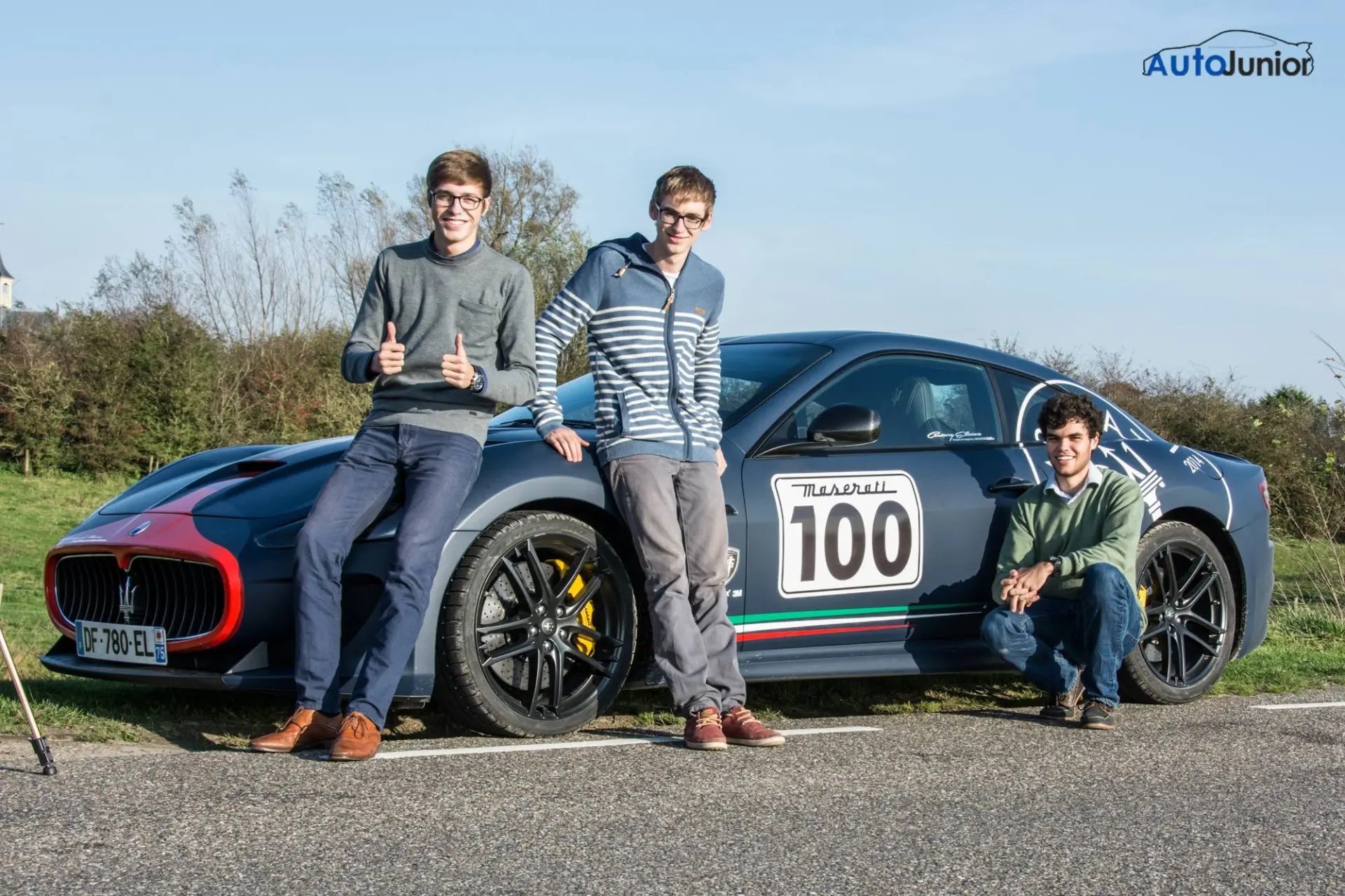 Three friends with a blue sports car wearing race number 100