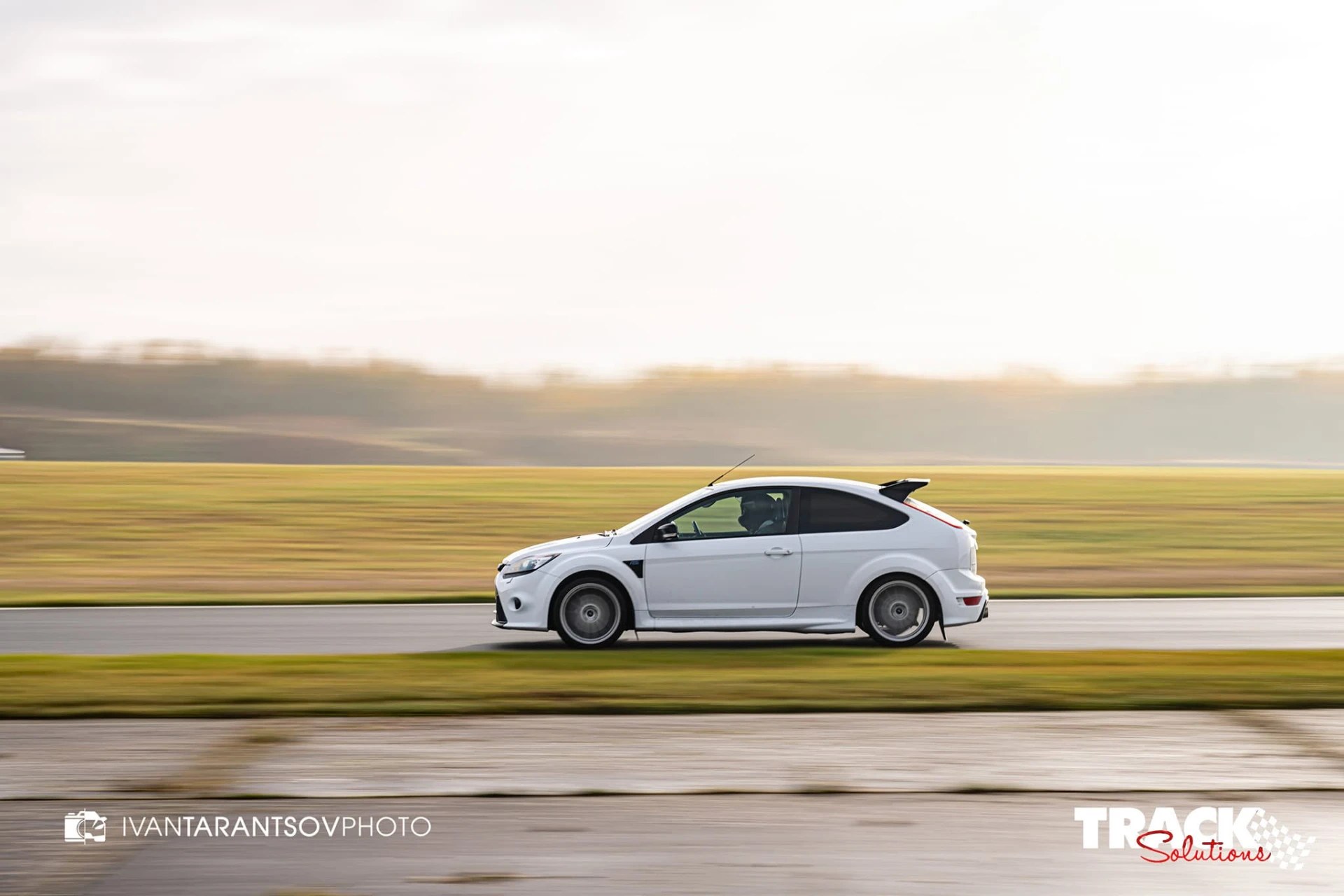 White hatchback on a race track, panning shot with motion-blurred wheels