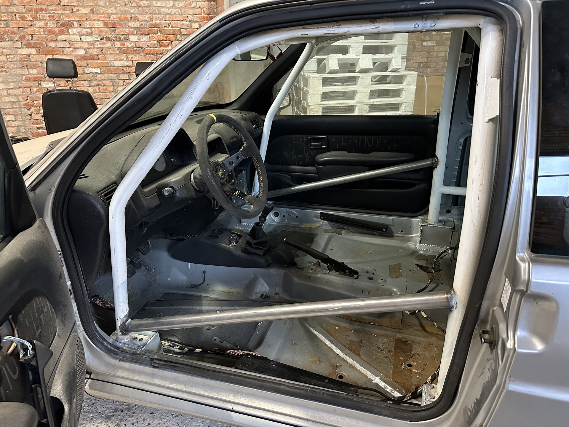 Stripped interior fitted with a roll cage and racing steering wheel in a brick workshop