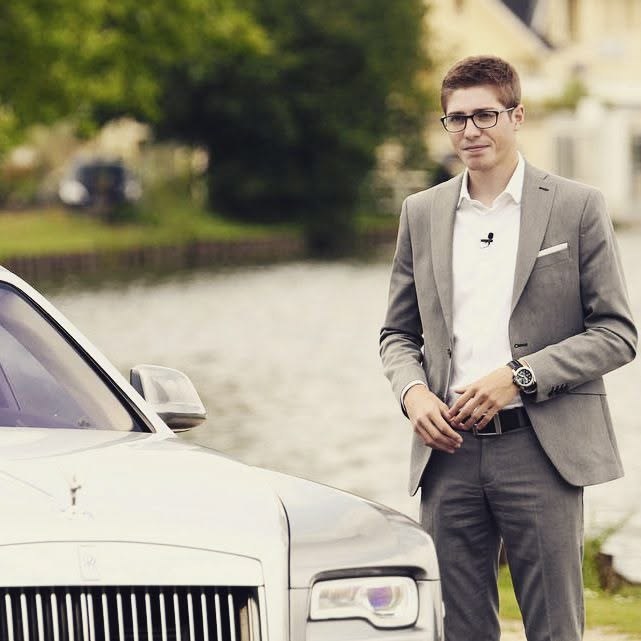 Louis in a grey suit next to a white luxury car