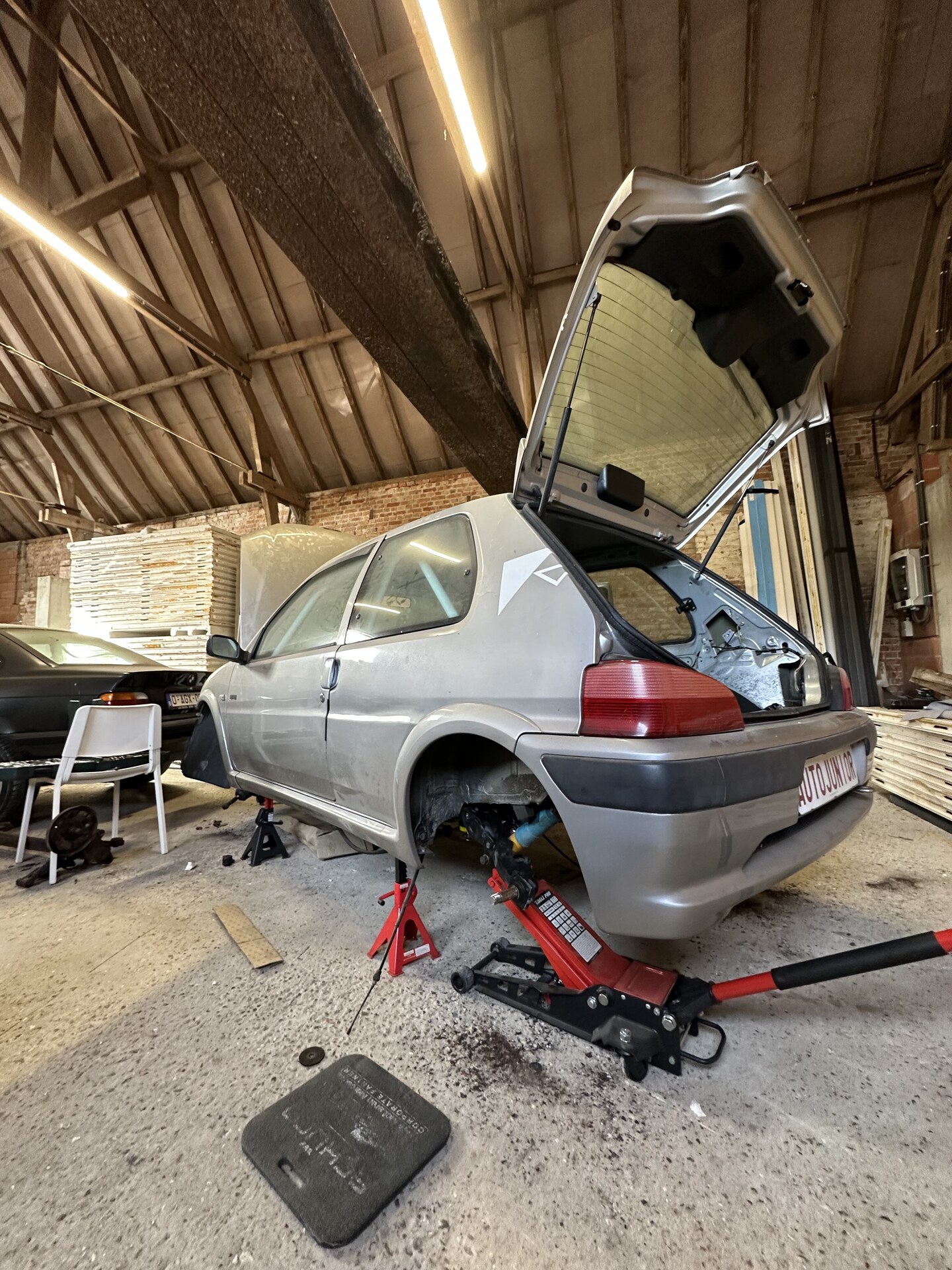 Rear of the car raised on jack stands in a workshop, hatch open and rear wheels removed