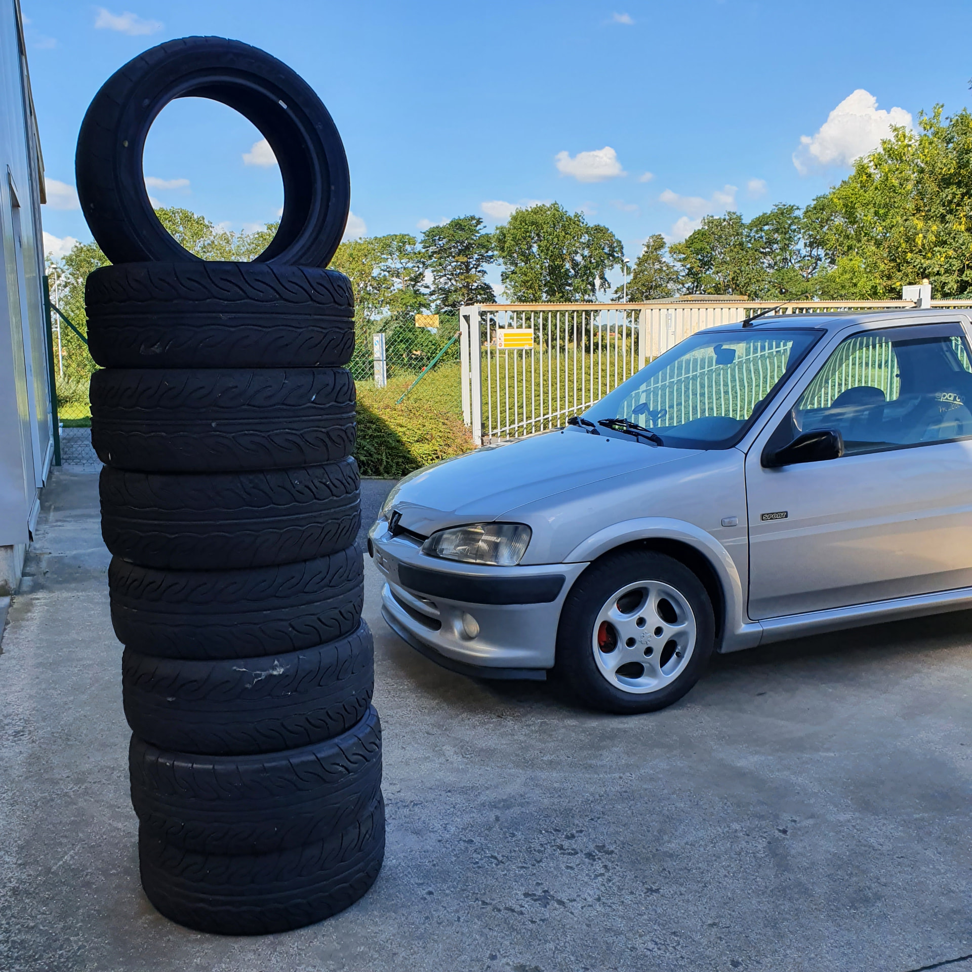 Silver Peugeot 106 parked beside a stack of tyres outside a workshop
