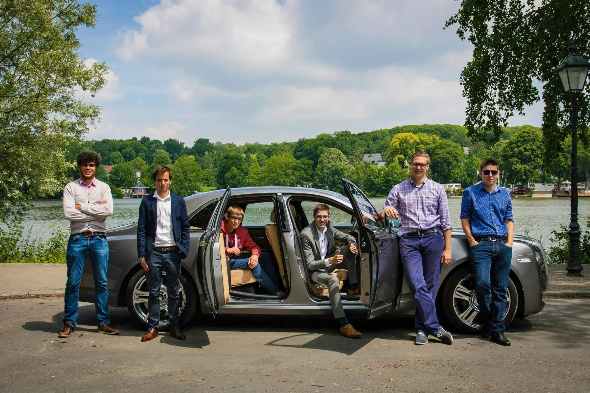 The AutoJunior team posing around a grey luxury saloon with its doors open